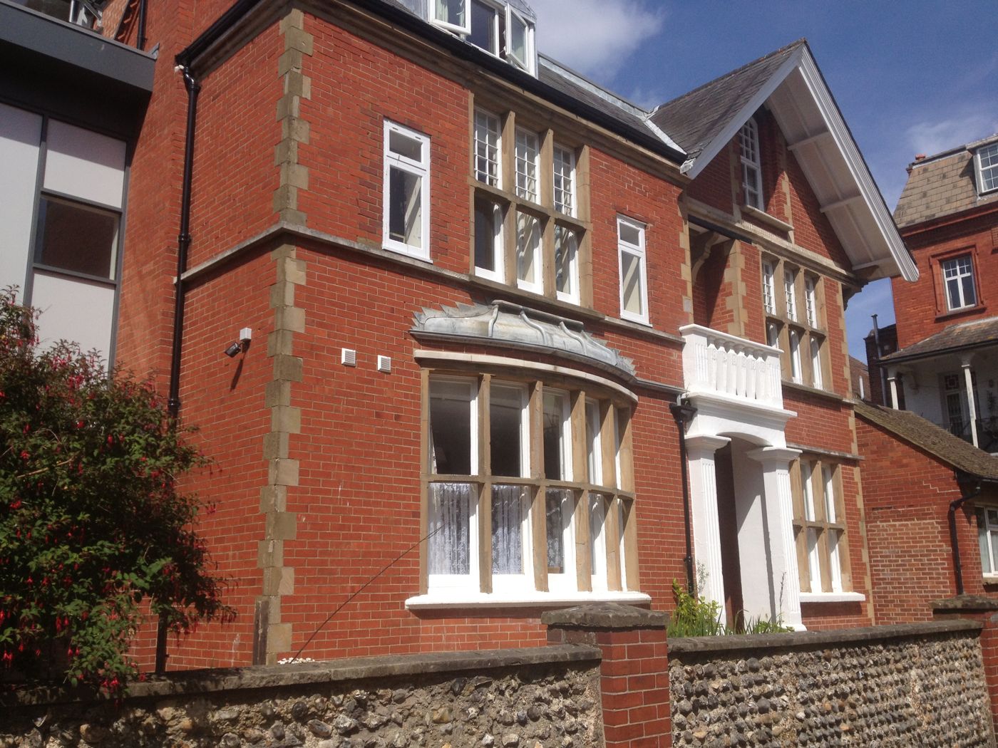 Large Victorian red-brick house with bay windows behind a flint wall