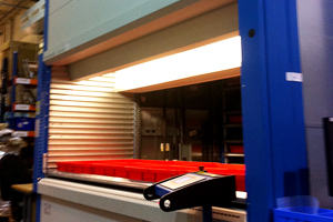 Lit automated storage unit with red trays inside a warehouse